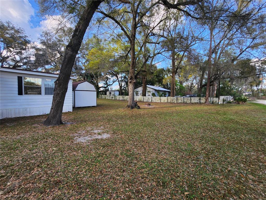 A grassy backyard features a white mobile home, a storage shed, and mature trees — 6091 SE 114TH STREET ROAD, BELLEVIEW, FL