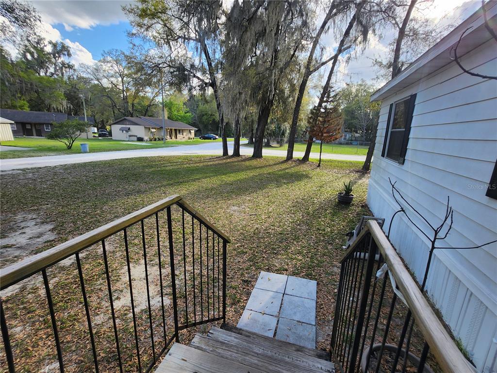 A view from wooden steps looking out over a grassy yard toward neighboring houses — 6091 SE 114TH STREET ROAD, BELLEVIEW, FL