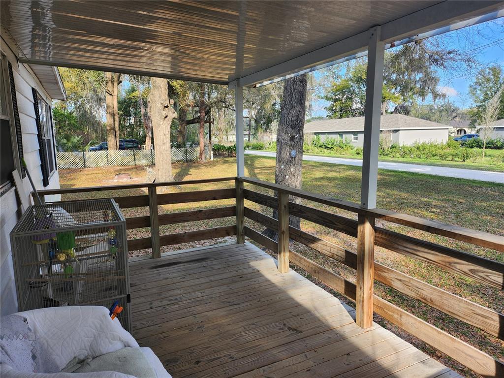 A covered wooden deck features a railing and a view of a grassy yard — 6091 SE 114TH STREET ROAD, BELLEVIEW, FL