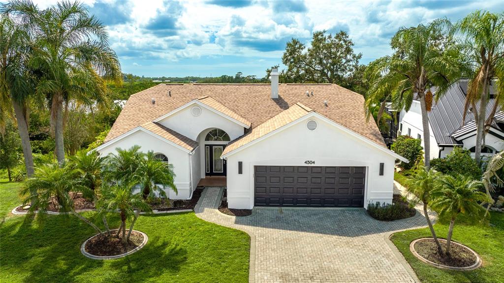 A white single-story house with a brown shingled roof, paved driveway, and palm trees — 4304 14TH AVENUE E, BRADENTON, FL