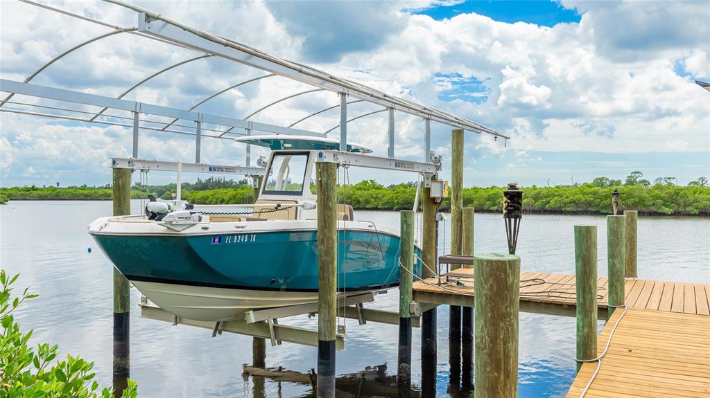 A teal motorboat is docked on a mechanical lift next to a wooden pier — 4304 14TH AVENUE E, BRADENTON, FL