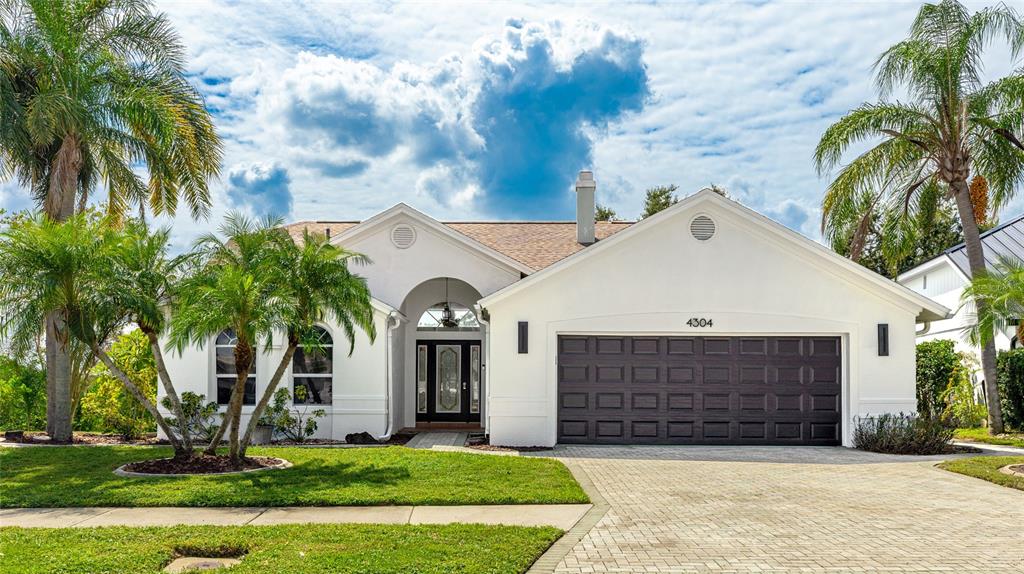 A white single-story house with a dark garage door and palm trees in the front yard — 4304 14TH AVENUE E, BRADENTON, FL