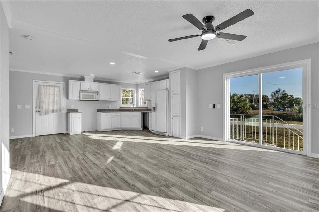 A bright, open-concept kitchen and living area with white cabinets, gray flooring, and sliding doors — 2610 CLYDE AVENUE, PUNTA GORDA, FL