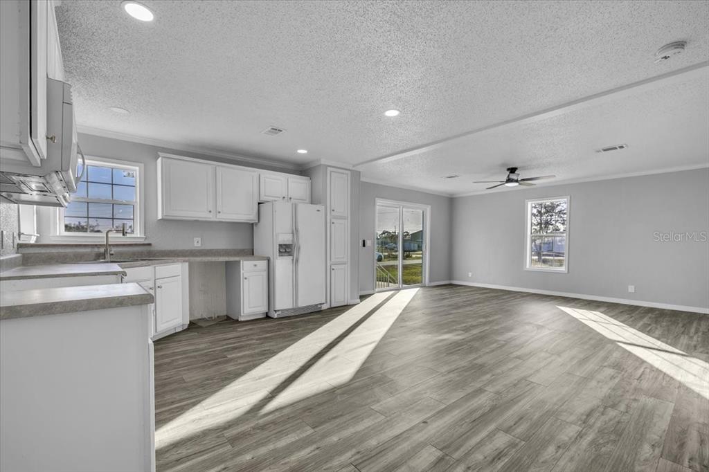 A kitchen and living area with white cabinets, light gray walls, and wood-look flooring — 2610 CLYDE AVENUE, PUNTA GORDA, FL