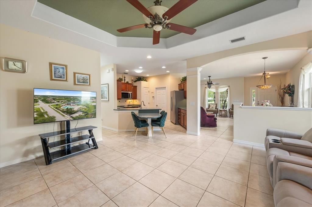A living room with tile floors, a tray ceiling, and an open view into the kitchen — 11409 56TH STREET CIRCLE E, PARRISH, FL