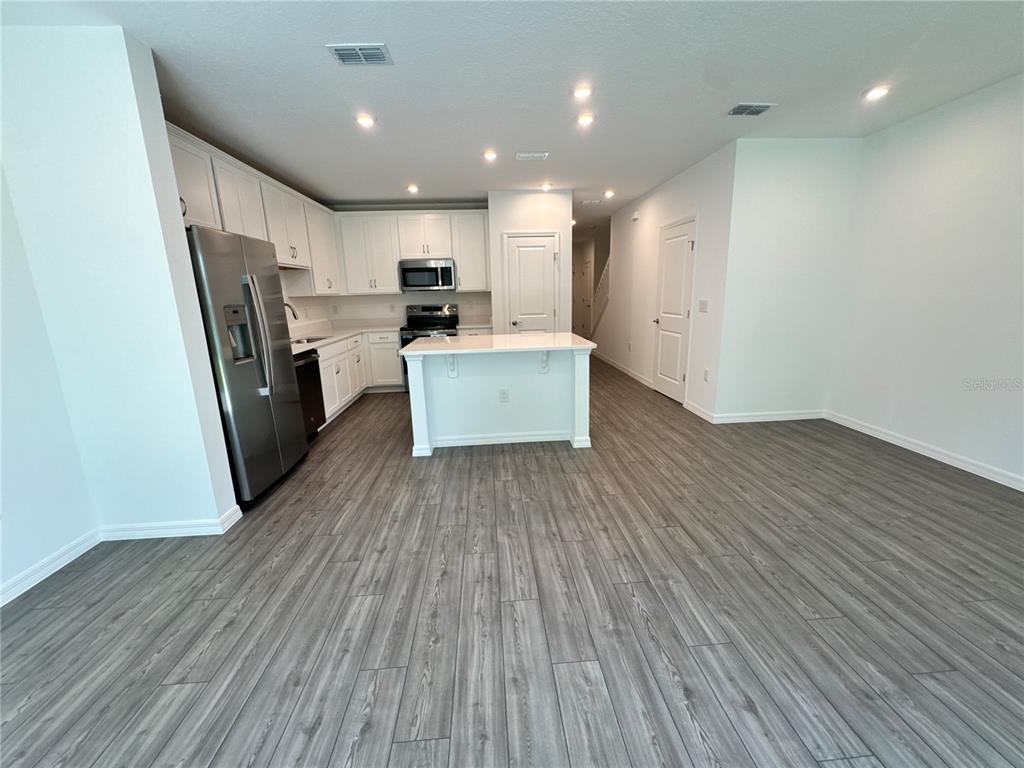 A kitchen features white cabinetry, stainless steel appliances, a center island, and gray wood-look flooring — 3031 JESSAMINE DRIVE, TAVARES, FL