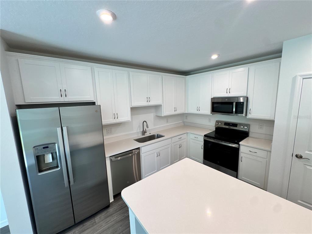 A kitchen features white cabinetry, stainless steel appliances, and a central island with quartz countertops — 3031 JESSAMINE DRIVE, TAVARES, FL