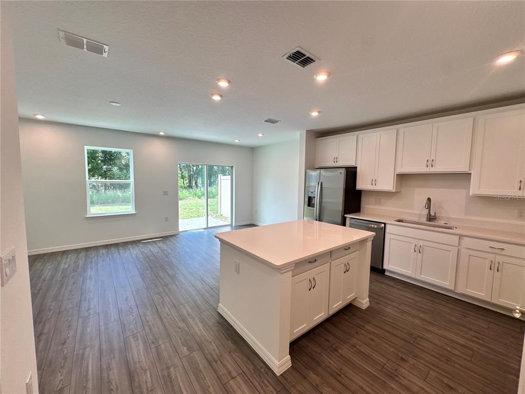 An open-concept kitchen and living area featuring white cabinets, a center island, and wood-look flooring — 3031 JESSAMINE DRIVE, TAVARES, FL