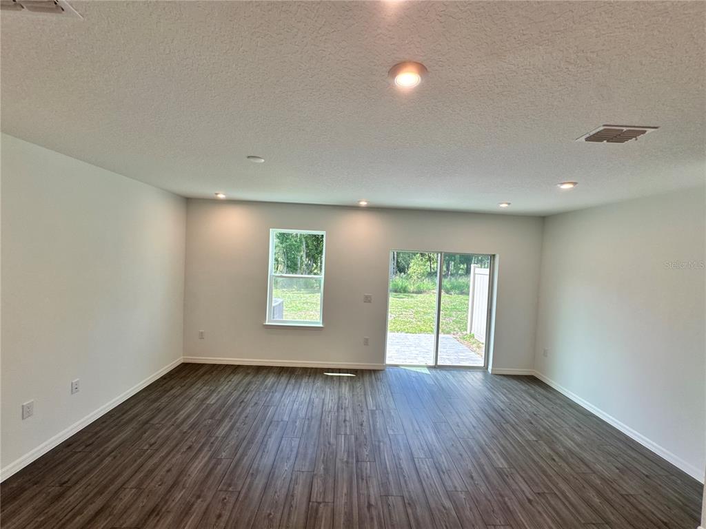An empty room with dark wood-look flooring, recessed lighting, a single window, and sliding doors — 3031 JESSAMINE DRIVE, TAVARES, FL