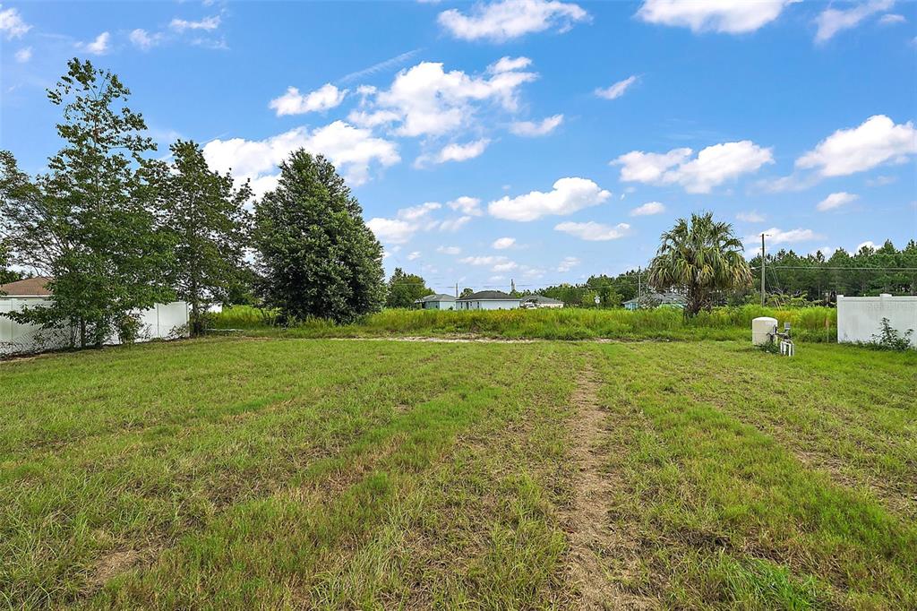 A grassy, vacant residential lot features scattered trees and a white vinyl fence — 23 OAK CIRCLE, OCALA, FL