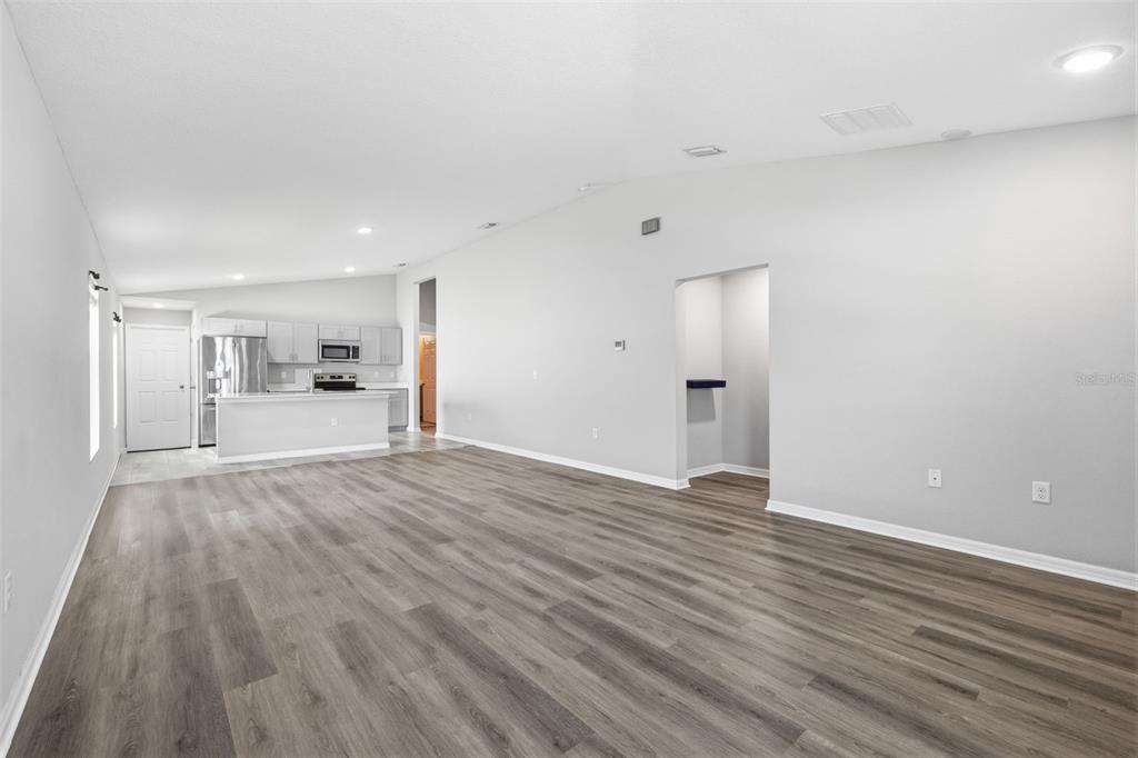 An open-concept living area with light gray walls, wood-look flooring, and an adjacent kitchen — 13011 PENNYBROOK DRIVE, RIVERVIEW, FL