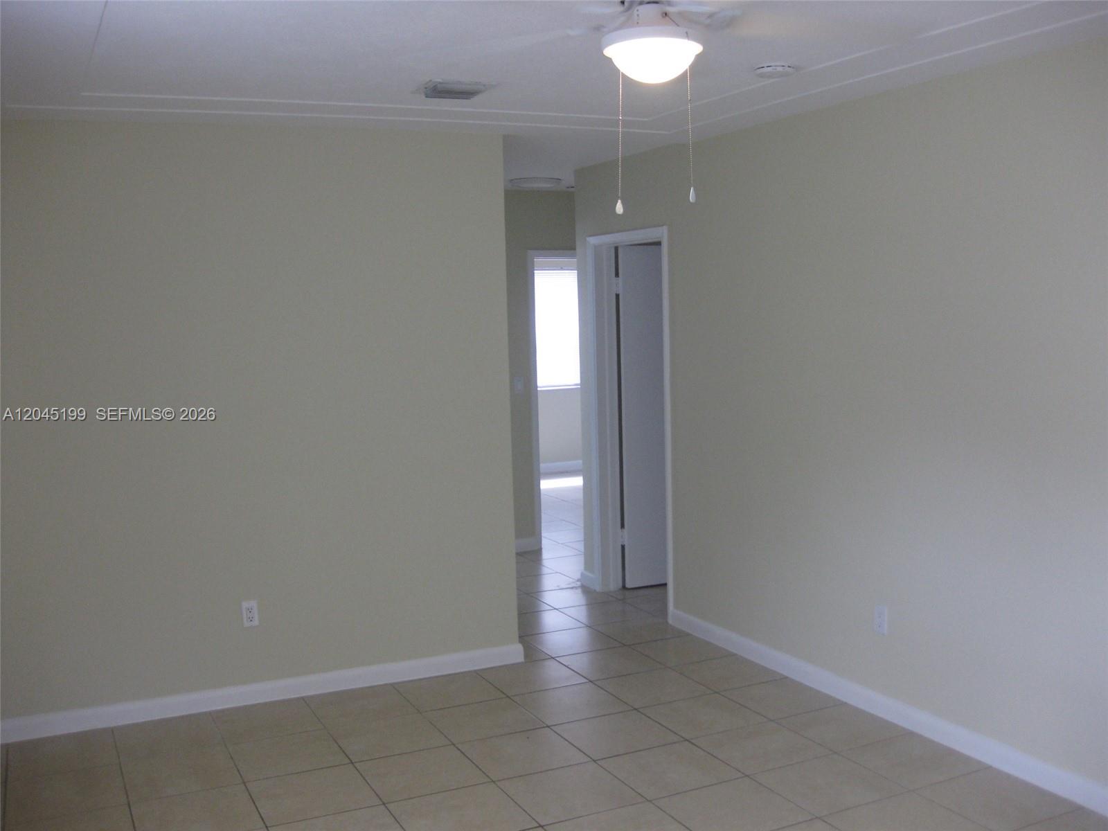 An interior view shows a room with beige walls, tile flooring, and a ceiling fan — 1520 NE 14th St, Homestead FL 33033, HOMESTEAD, FL