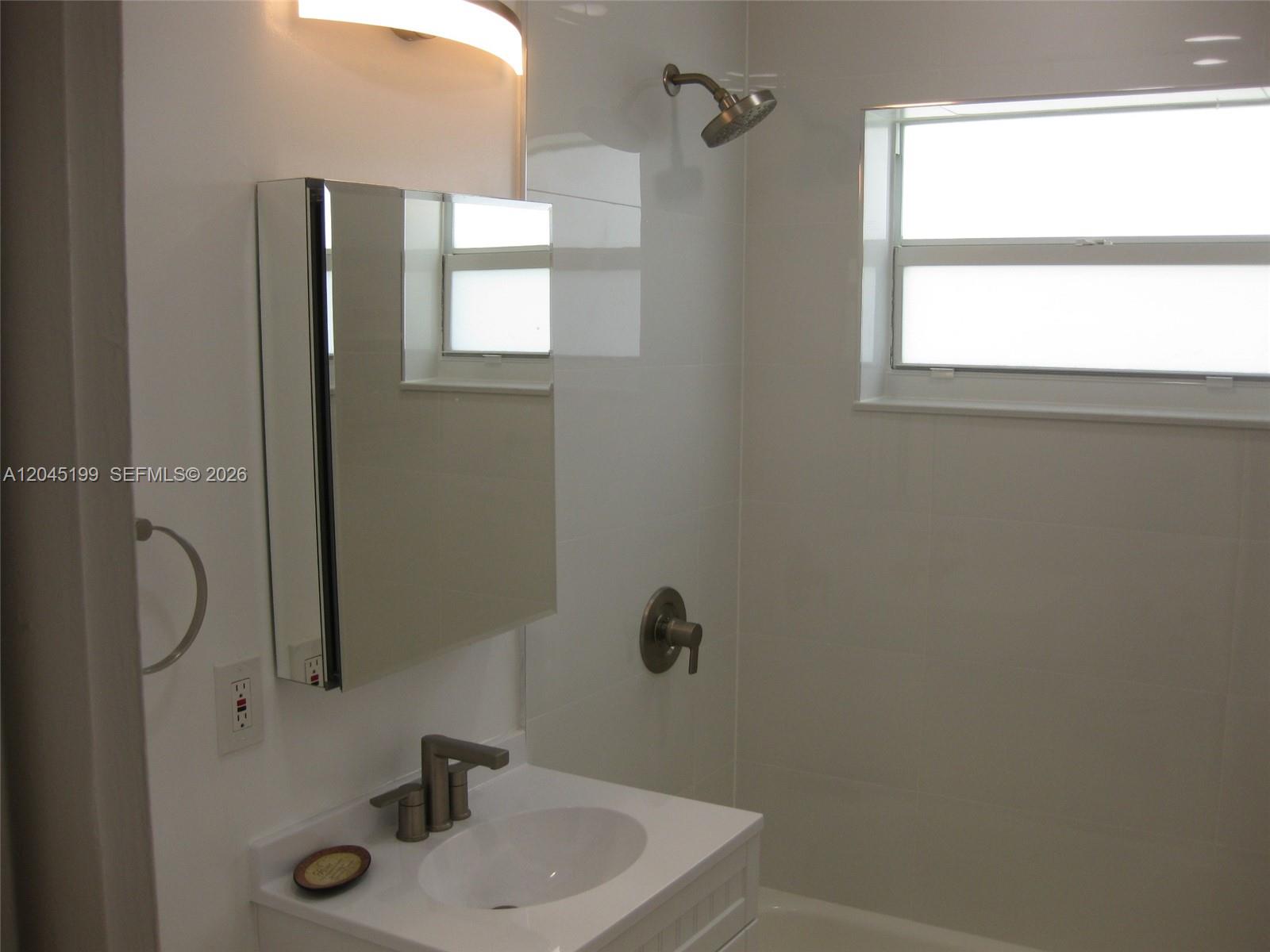 A bathroom features a white vanity, a mirrored medicine cabinet, and a tiled shower area — 1520 NE 14th St, Homestead FL 33033, HOMESTEAD, FL