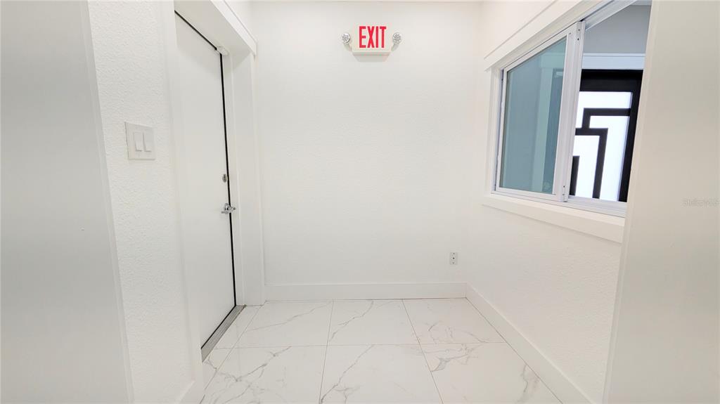 A small, white-walled room with marble-patterned tile flooring, a white door, and an exit sign — 1245 N PINE HILLS ROAD, ORLANDO, FL