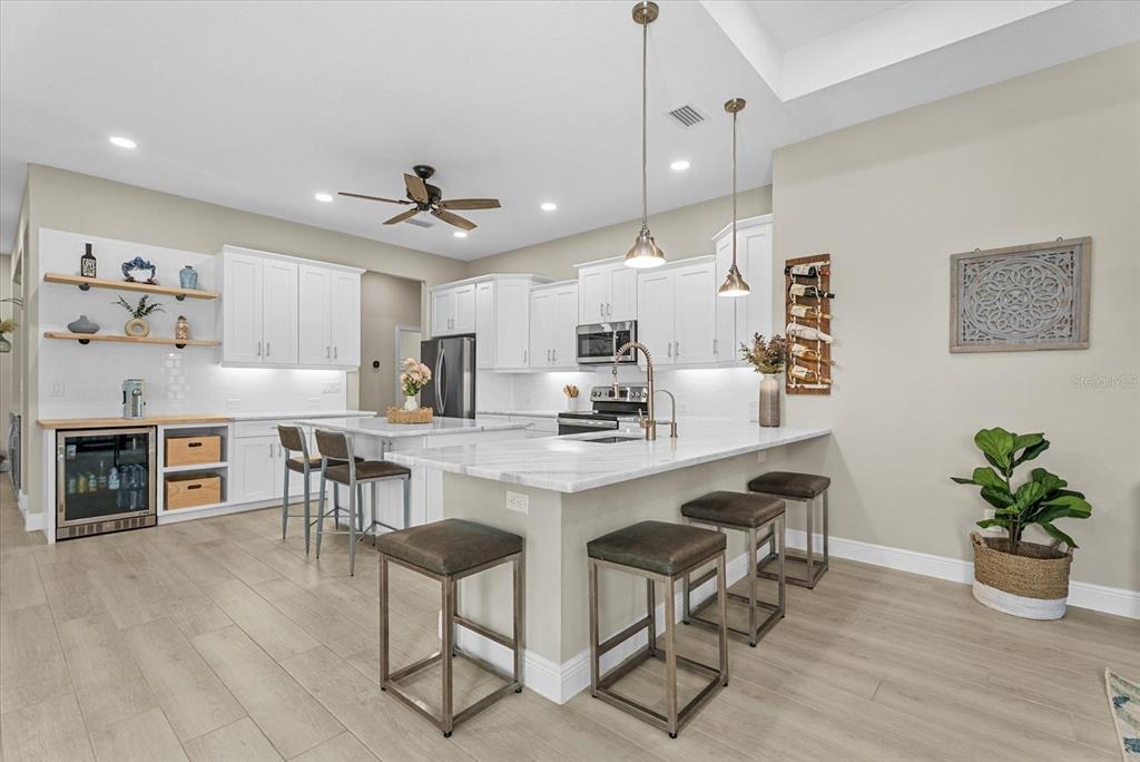 A modern kitchen features white cabinetry, marble countertops, a central island, and light wood flooring — 489 ARBORVIEW LANE, VENICE, FL