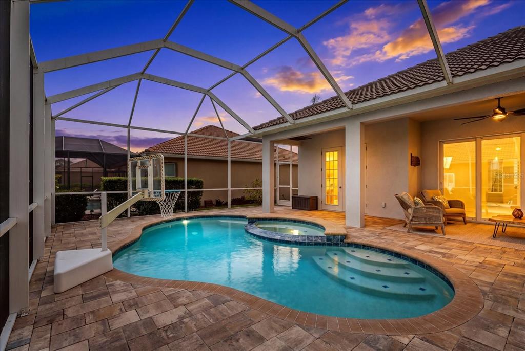 A screened-in patio features a swimming pool, a spa, and a basketball hoop at sunset — 489 ARBORVIEW LANE, VENICE, FL