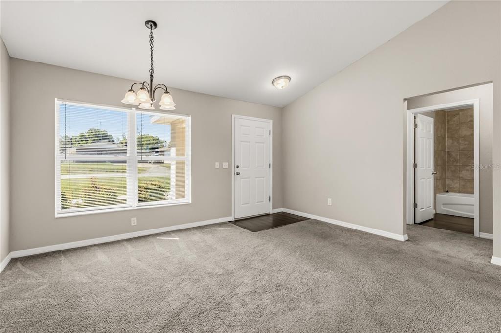 A carpeted room with a chandelier, a front door, and a doorway leading to a bathroom — 5223 SE 135TH PLACE, SUMMERFIELD, FL