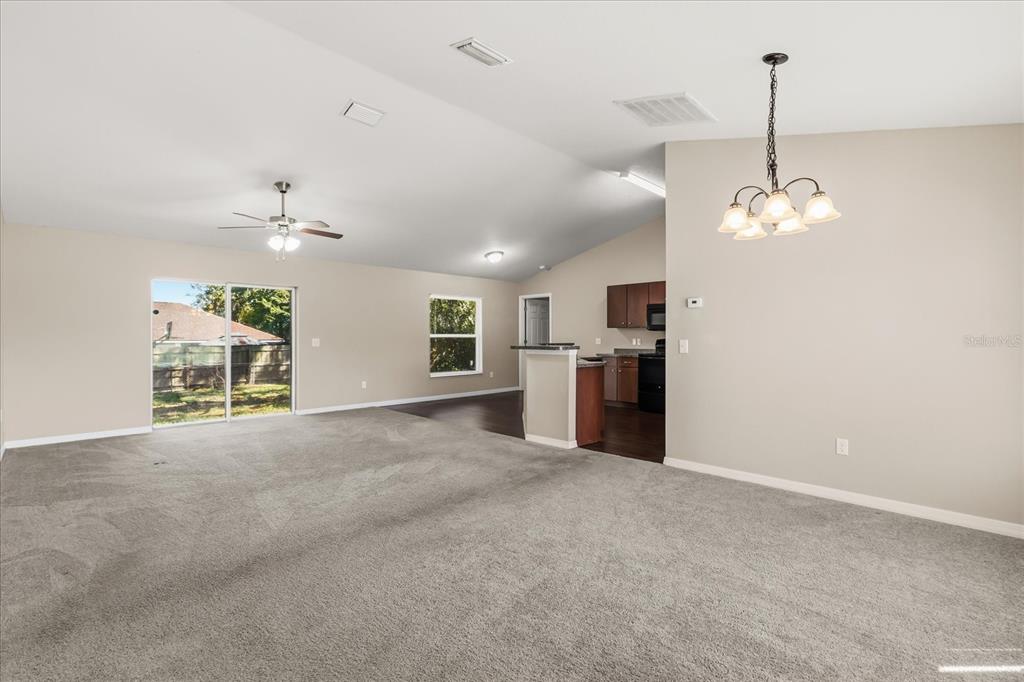 A spacious living room with gray carpeting, vaulted ceilings, and an adjacent open kitchen — 5223 SE 135TH PLACE, SUMMERFIELD, FL