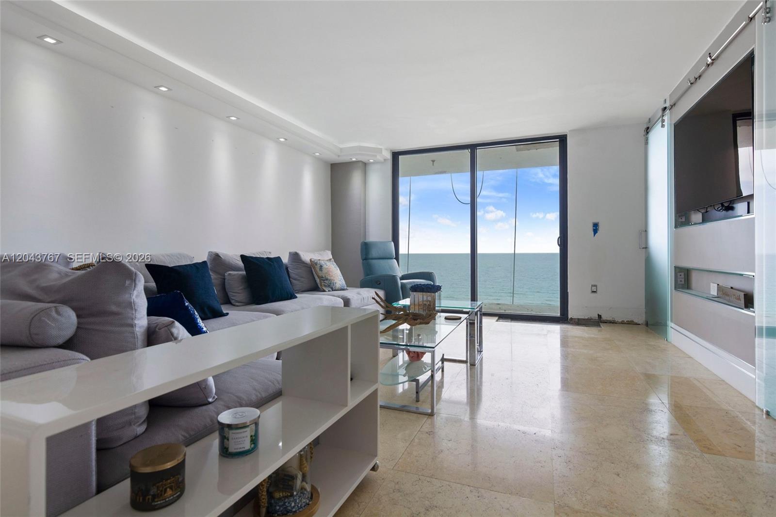 A living room features a grey sectional sofa, glass coffee tables, and floor-to-ceiling ocean views — 6061 Collins Ave # 8F, Miami Beach FL 33140, MIAMI BEACH, FL