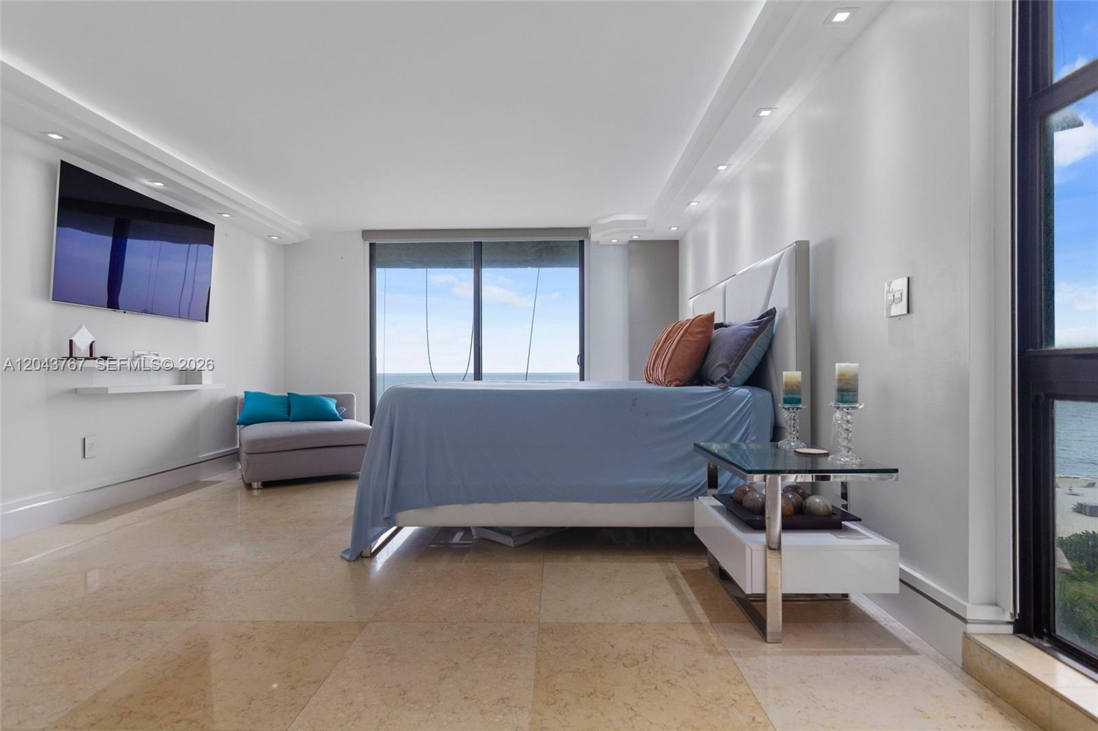 A bedroom features a bed, a gray chaise lounge, and a view of the ocean — 6061 Collins Ave # 8F, Miami Beach FL 33140, MIAMI BEACH, FL