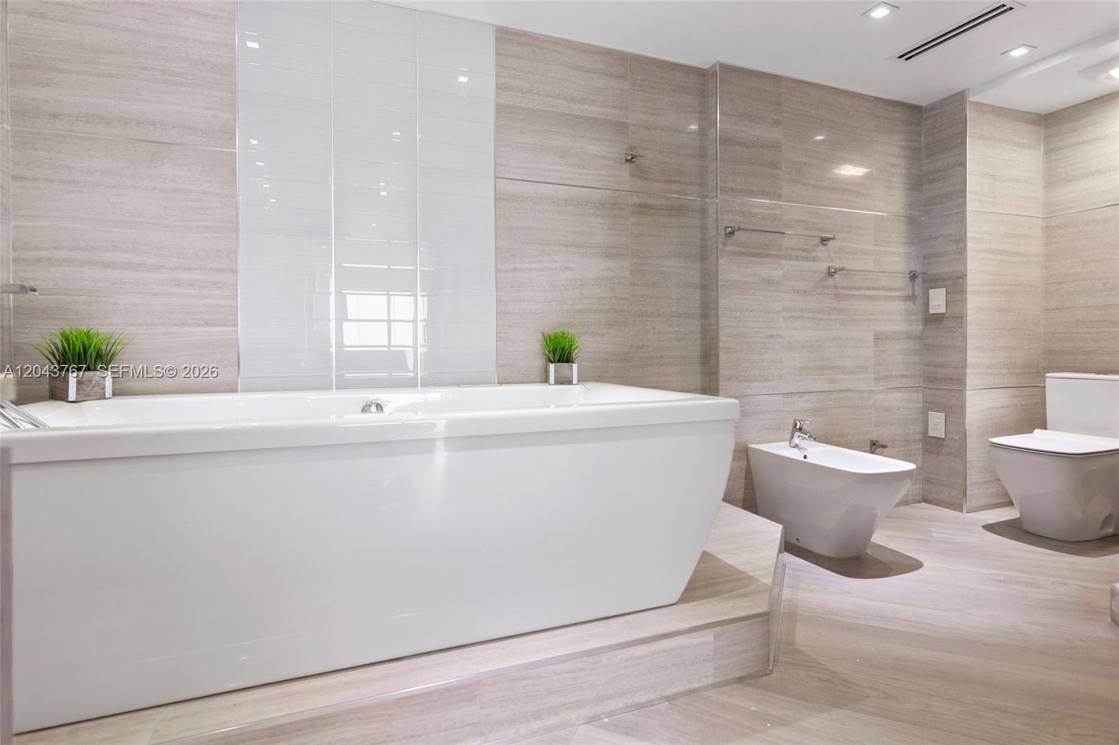 A modern bathroom features a white soaking tub, a bidet, and a toilet with beige tile — 6061 Collins Ave # 8F, Miami Beach FL 33140, MIAMI BEACH, FL