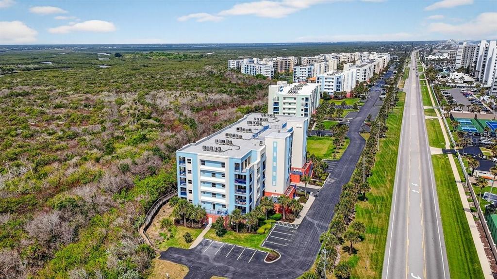 An aerial view shows a multi-story apartment building next to a road and dense vegetation — 5300 S ATLANTIC AVENUE UNIT 19-203, NEW SMYRNA BEACH, FL