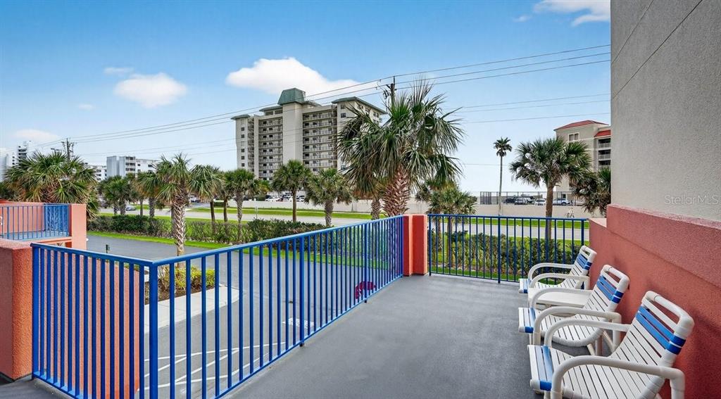 A balcony with blue railings and white lounge chairs overlooks a parking lot and palms — 5300 S ATLANTIC AVENUE UNIT 19-203, NEW SMYRNA BEACH, FL