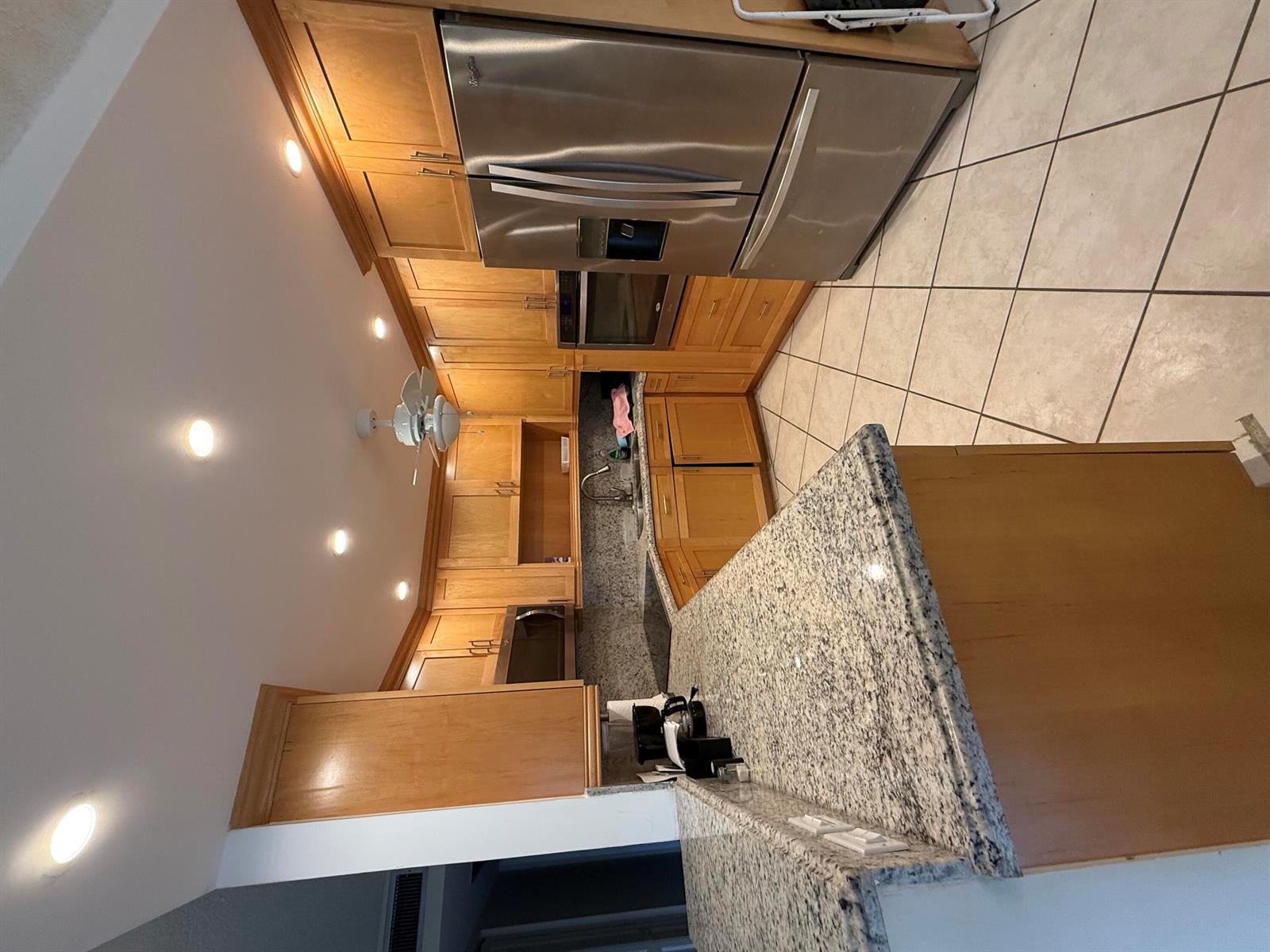 A kitchen features light wood cabinets, granite countertops, stainless steel appliances, and tile flooring — 1046 Wolverton C, Boca Raton FL 33434, BOCA RATON, FL