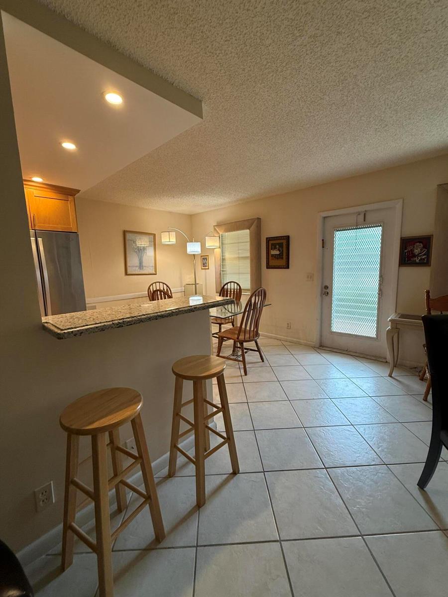 A kitchen with a granite breakfast bar, wooden stools, and an adjacent dining area — 1046 Wolverton C, Boca Raton FL 33434, BOCA RATON, FL