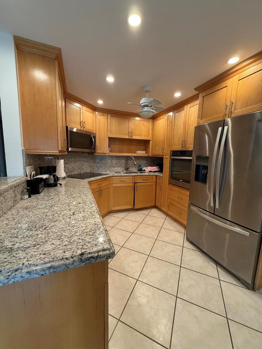 A kitchen with light wood cabinets, granite countertops, stainless steel appliances, and diagonal tile flooring — 1046 Wolverton C, Boca Raton FL 33434, BOCA RATON, FL