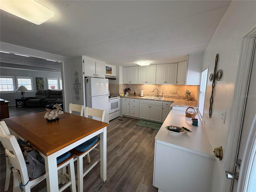 A kitchen with white cabinets, wood-look flooring, and an adjacent dining area with a table — 408 49TH A AVENUE E, BRADENTON, FL