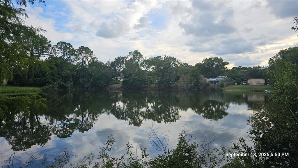 A view of a calm pond surrounded by trees and residential houses under a cloudy sky — 691 PIEDMONT DRIVE, DELTONA, FL