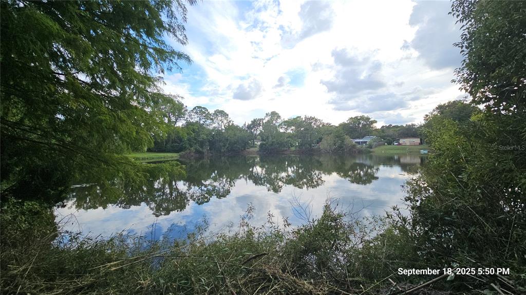 A view of a calm pond surrounded by trees and distant houses under a cloudy sky — 691 PIEDMONT DRIVE, DELTONA, FL