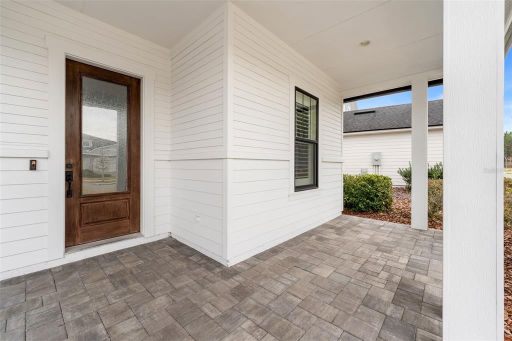 A covered front porch features white horizontal siding, a wood-framed glass door, and paver flooring — 11081 SW 38TH BOULEVARD, GAINESVILLE, FL