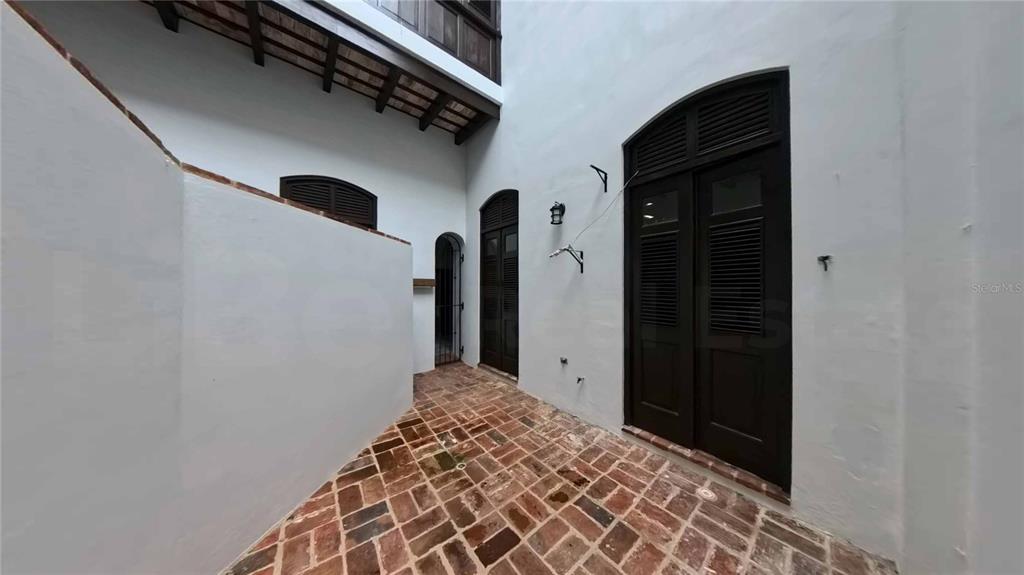 A narrow outdoor courtyard features white walls, dark wooden doors, and a red brick floor — 152 SAN JUSTO STREET, SAN JUAN, PR
