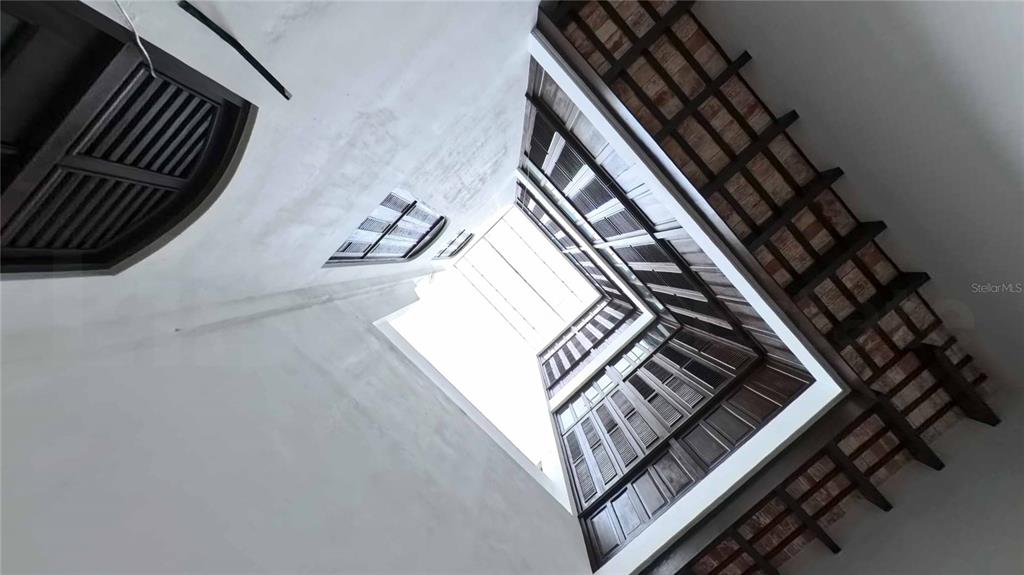 A low-angle view looking up through a multi-story interior atrium with dark wooden shutters — 152 SAN JUSTO STREET, SAN JUAN, PR