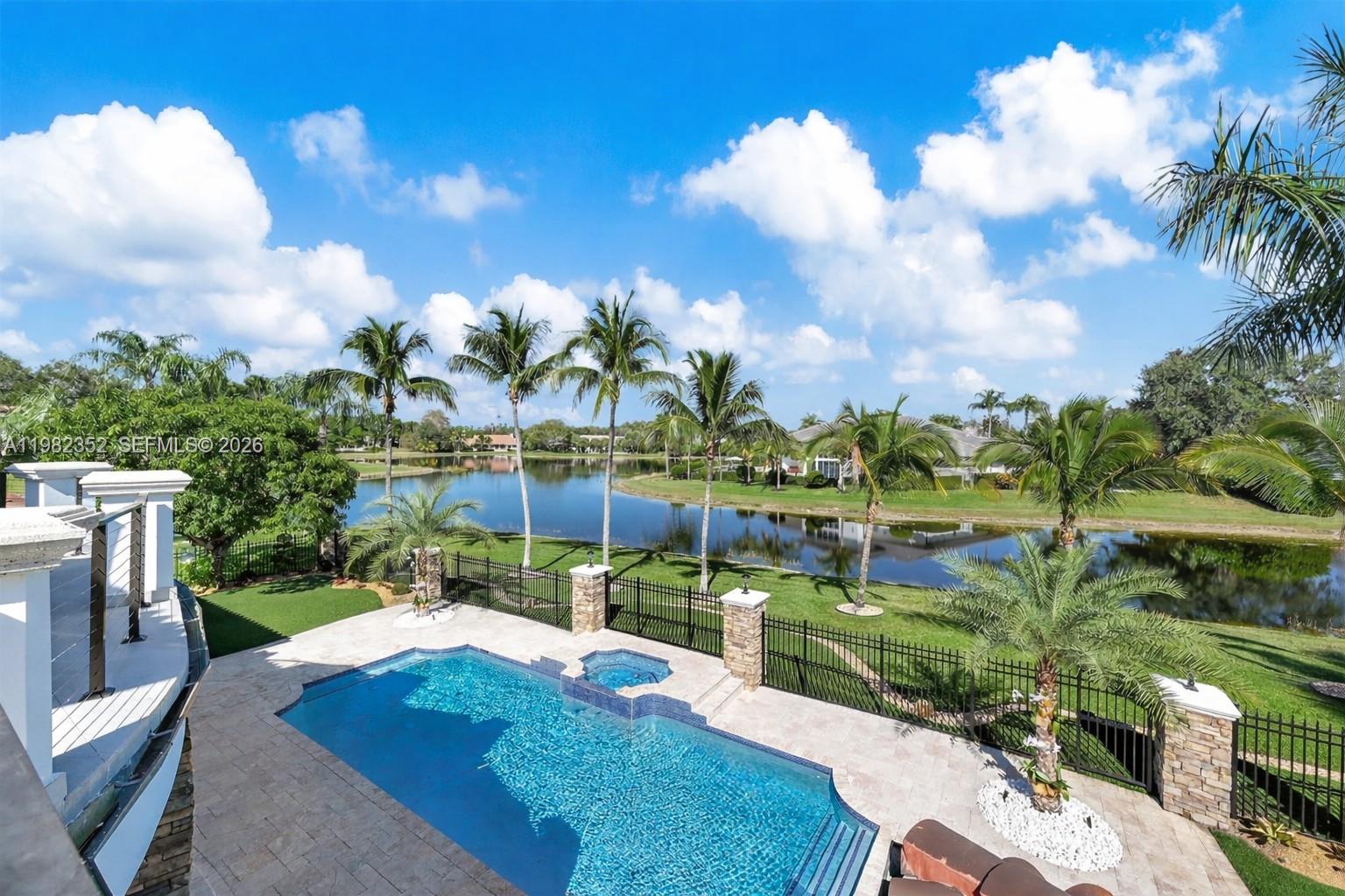 An elevated view of a swimming pool and spa overlooking a lake and palm trees — 2905 Paddock Rd, Weston FL 33331, WESTON, FL