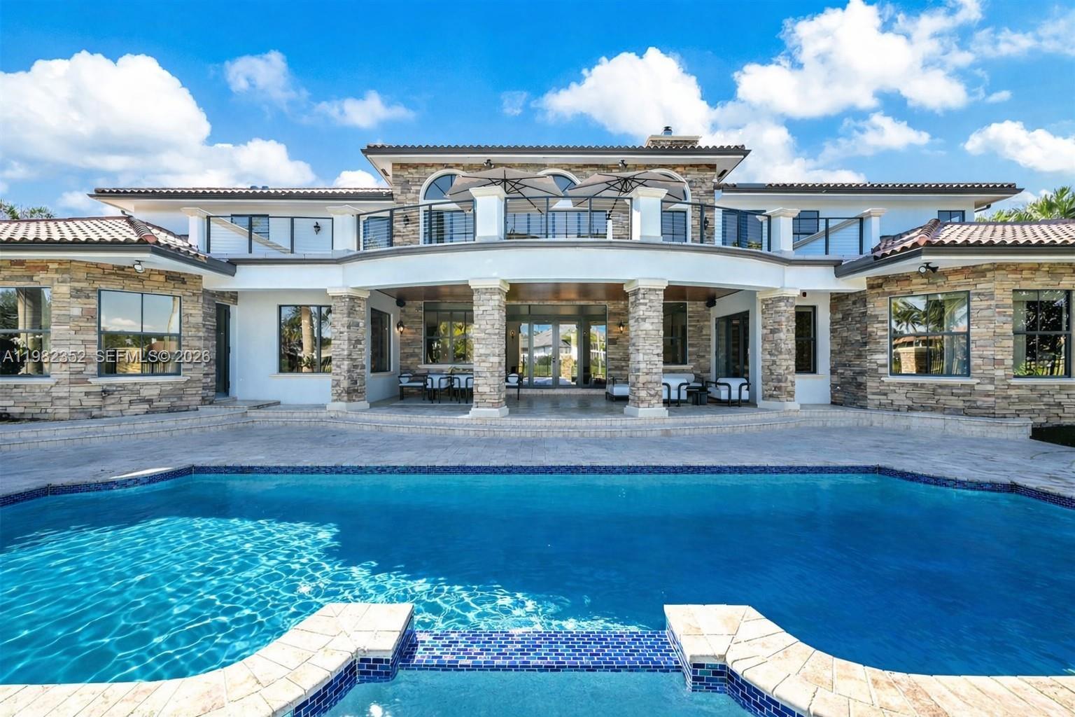 An outdoor swimming pool and spa overlook a lake with palm trees and a fence — 2905 Paddock Rd, Weston FL 33331, WESTON, FL