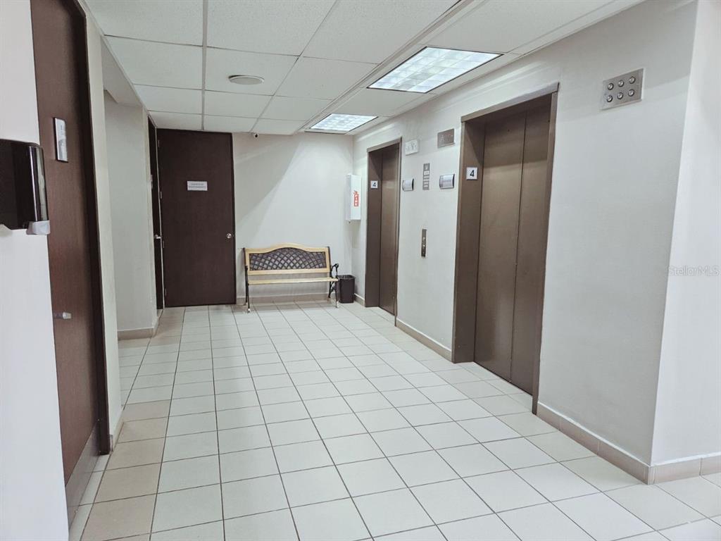 An elevator lobby features tiled floors, a wooden bench, and two elevator doors — 57 SANTA CRUZ UNIT 1, BAYAMON, PR