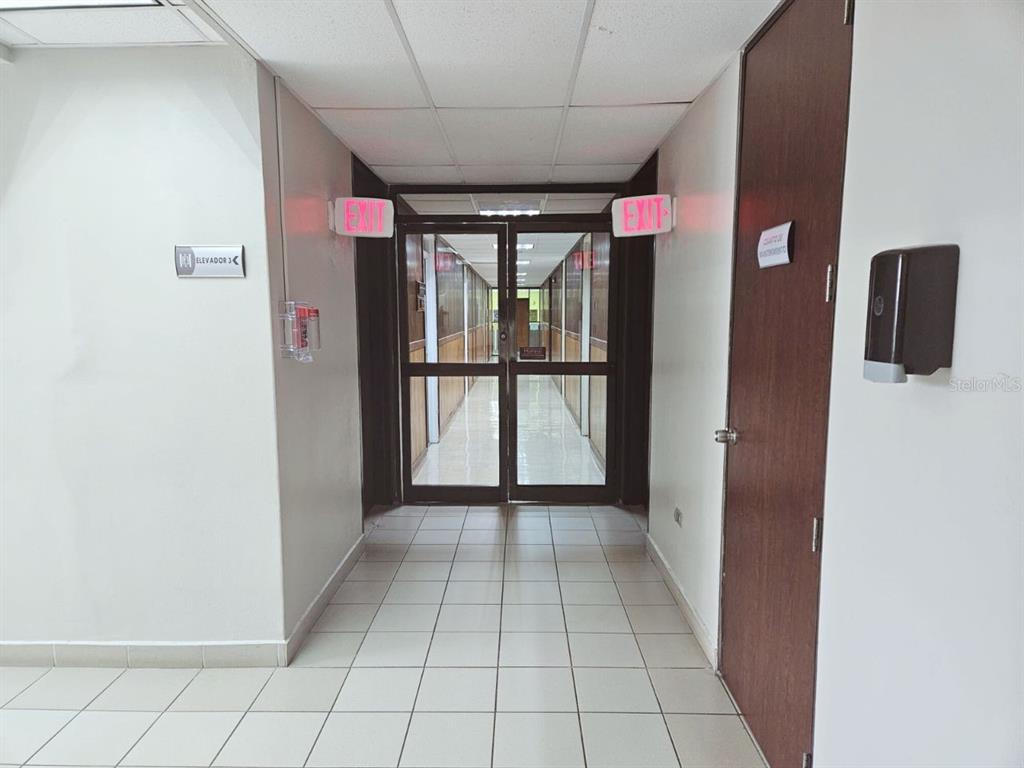 A tiled hallway leads to a glass-paneled double door with red exit signs above — 57 SANTA CRUZ UNIT 1, BAYAMON, PR