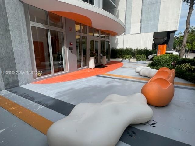 An exterior view of a building entrance featuring modern, organic-shaped seating on a paved patio — 31 SE 6th St # 1606, Miami FL 33131, MIAMI, FL