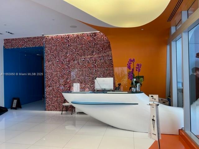 A modern reception area features a white curved desk, patterned wall, and orange accent wall — 31 SE 6th St # 1606, Miami FL 33131, MIAMI, FL