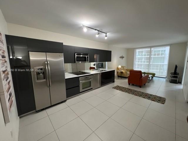 A modern kitchen with stainless steel appliances and dark cabinetry opens into a living area — 31 SE 6th St # 1606, Miami FL 33131, MIAMI, FL