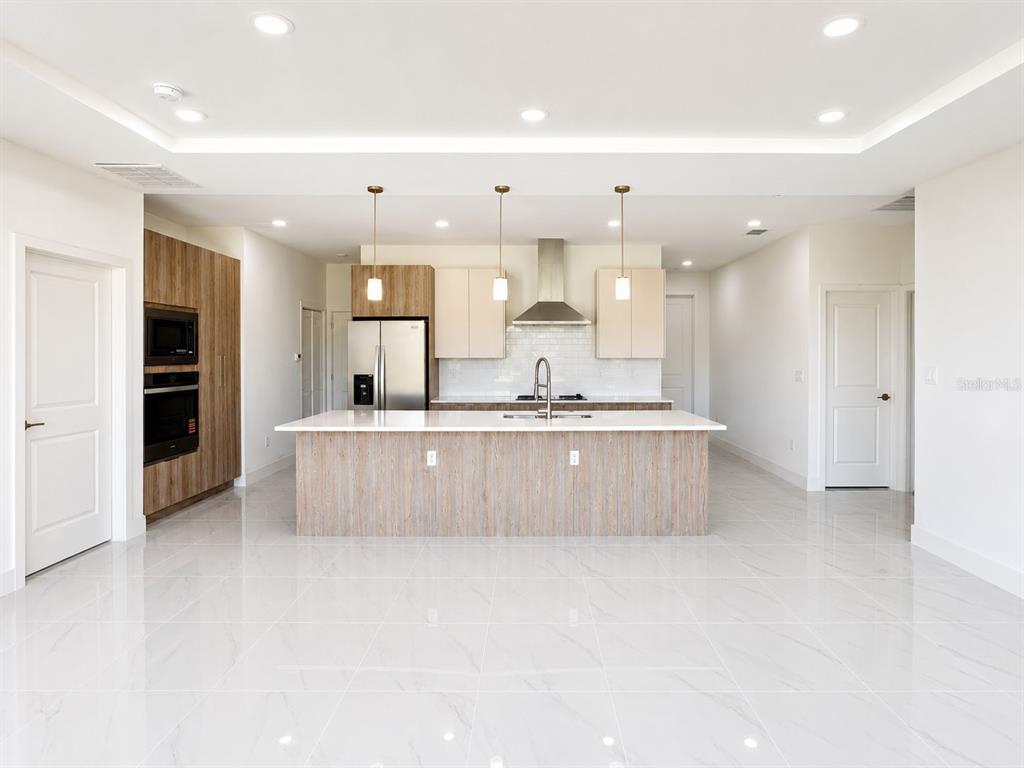 A modern kitchen features a large island, stainless steel appliances, and light-colored tile flooring — 117 NW 13TH STREET, CAPE CORAL, FL