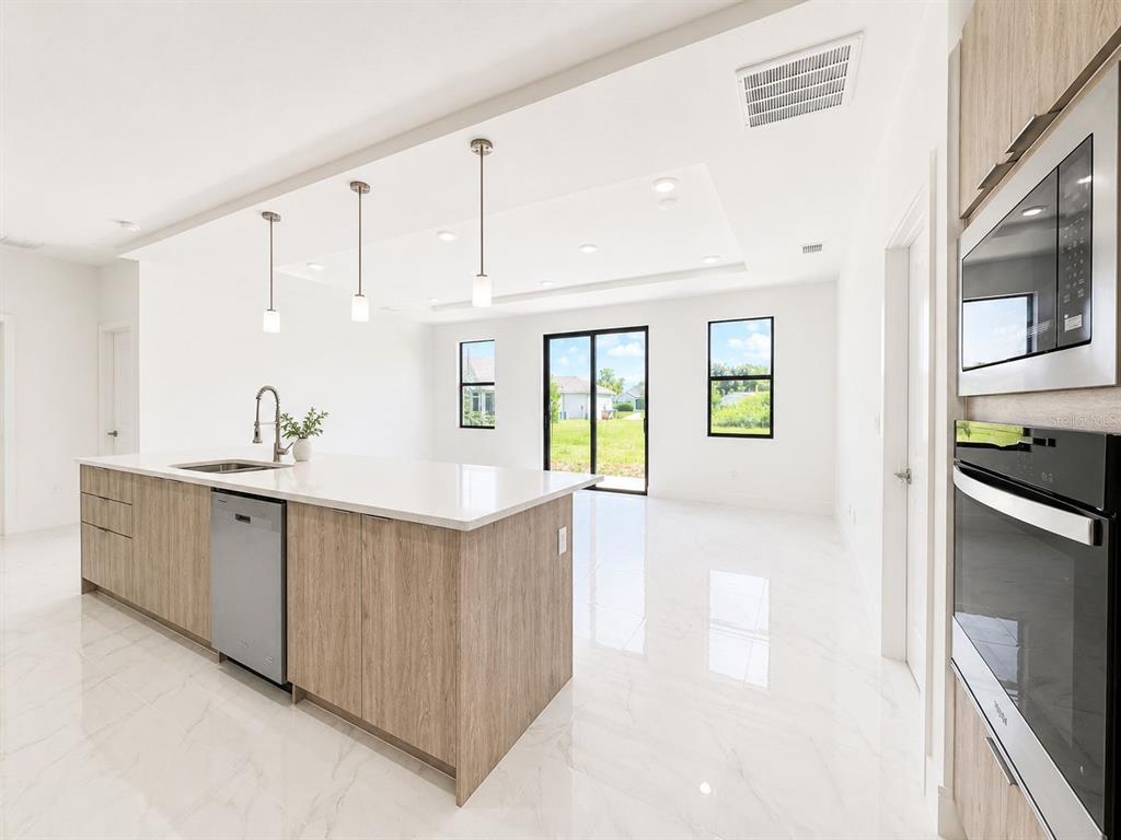 A modern kitchen features light wood cabinets, a white quartz island, and white tile flooring — 117 NW 13TH STREET, CAPE CORAL, FL