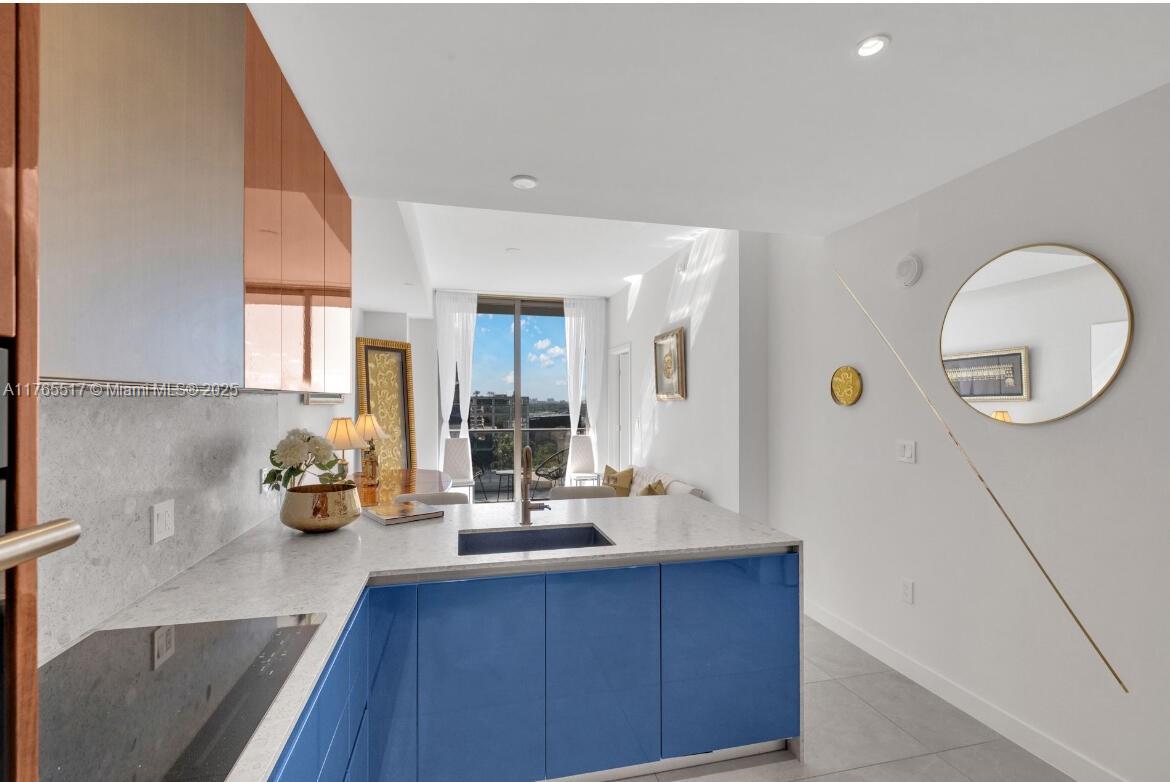 A modern kitchen features blue cabinets, a stone countertop, and an open view of a balcony — 2678 Tigertail # 1009, Miami FL 33133, MIAMI, FL