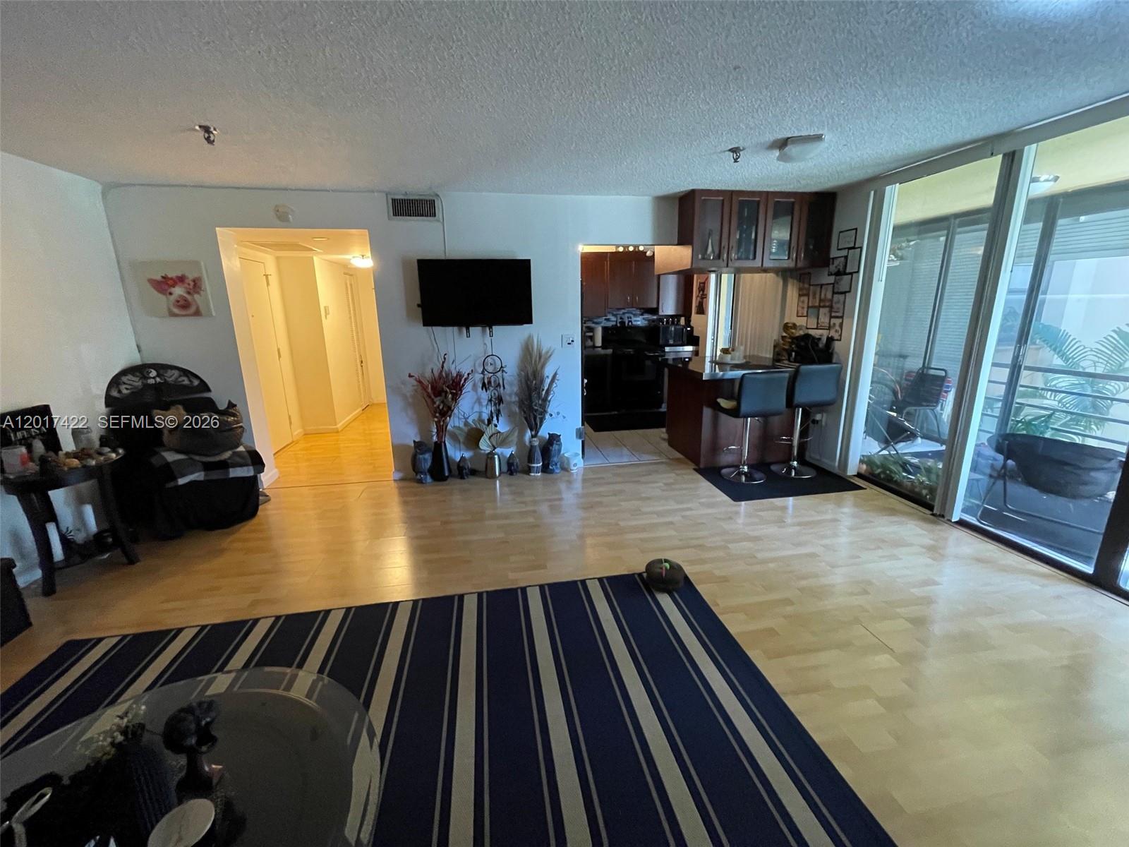 This living room features light wood flooring, a striped area rug, and an open kitchen — 671 NE 195th St, Miami FL 33179, MIAMI, FL