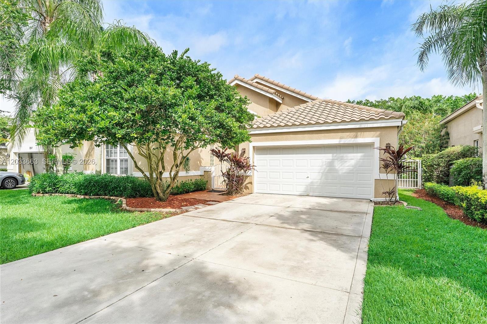 A tan house with a white garage door, a concrete driveway, and a large tree — 2013 Island Cir, Weston FL 33326, WESTON, FL