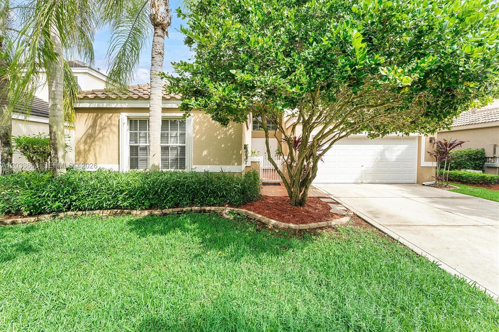 A single-story house with a tan stucco exterior, a two-car garage, and a front lawn — 2013 Island Cir, Weston FL 33326, WESTON, FL