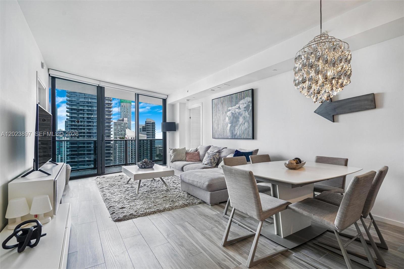 A modern living and dining room features a chandelier, white furniture, and floor-to-ceiling windows — 801 S Miami Ave # 4302, Miami FL 33130, MIAMI, FL